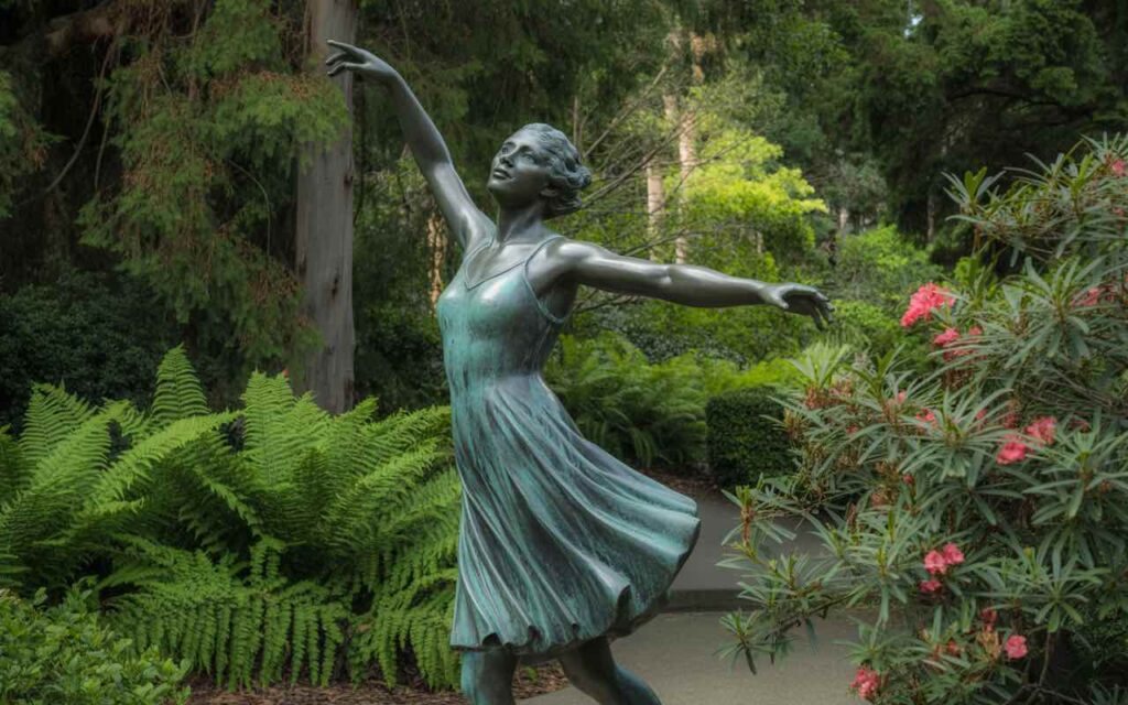 A stunning scene in the botanical gardens, where a bronze-style sculpture of a dancing woman is beautifully set among the lush plants and trees. Perfectly capturing the harmony between gardens and galleries.